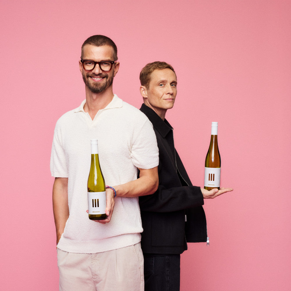 III Freunde Wein gehalten von Joko Winterscheidt und Mathias Schweighöfer vor rosa Hintergrund