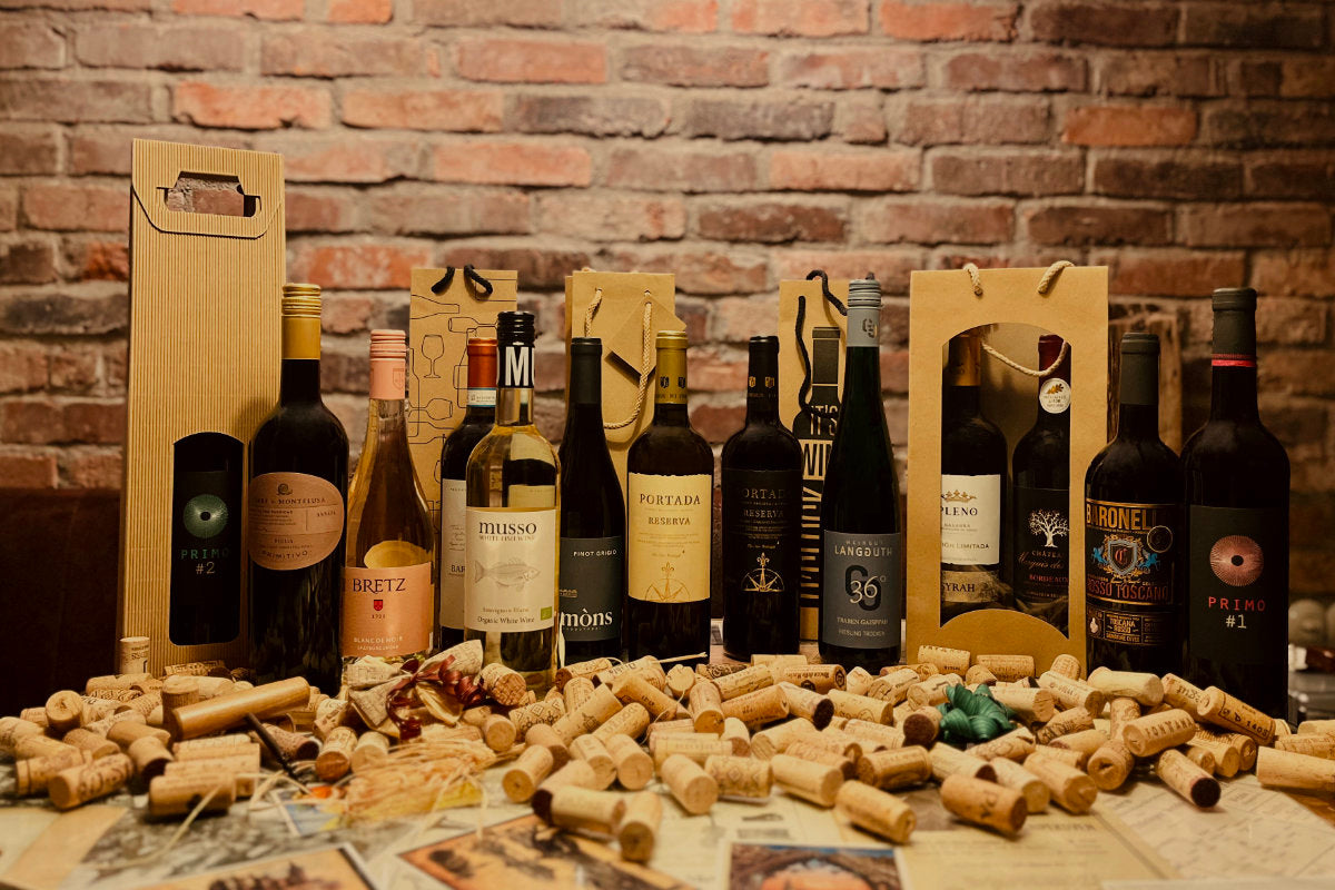 Kategoriebild Wein Geschenk verschiedene Weinflaschen auf Tisch mit Korken vor Backsteinwand mit Geschenktüten