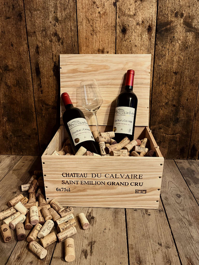 2 Flaschen Chateau Du Calvaire Saint Emilion Grand Cru Rotwein Trocken in düsterer Atmosphäre in einer Holzkiste mit Korken und einem Weinglas