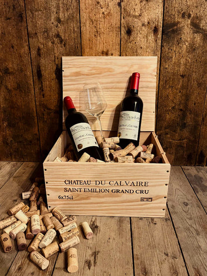 2 Flaschen Chateau Du Calvaire Saint Emilion Grand Cru Rotwein Trocken in düsterer Atmosphäre in einer Holzkiste mit Korken und einem Weinglas