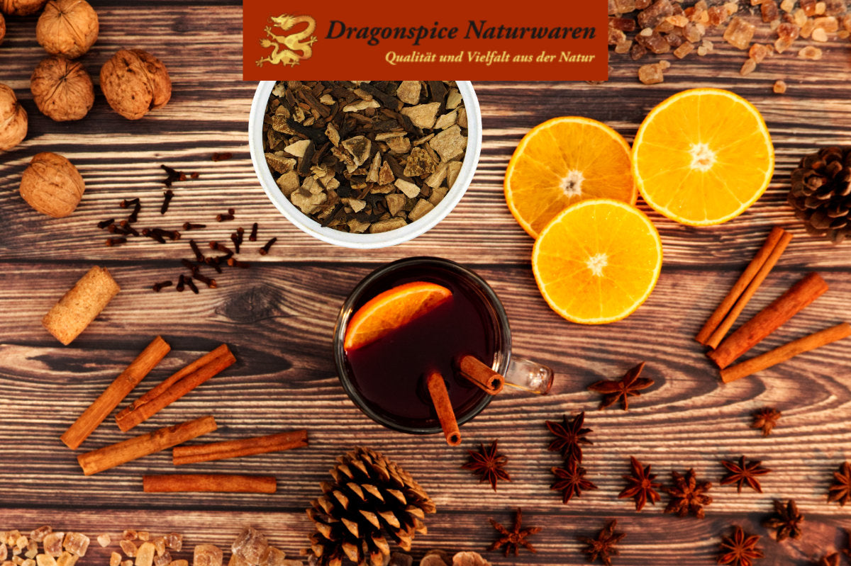 Glühweingewürz von Dragon Spice umrahmt von Orangenscheiben, Nelken und Zimt und einer Tasse Glühwein